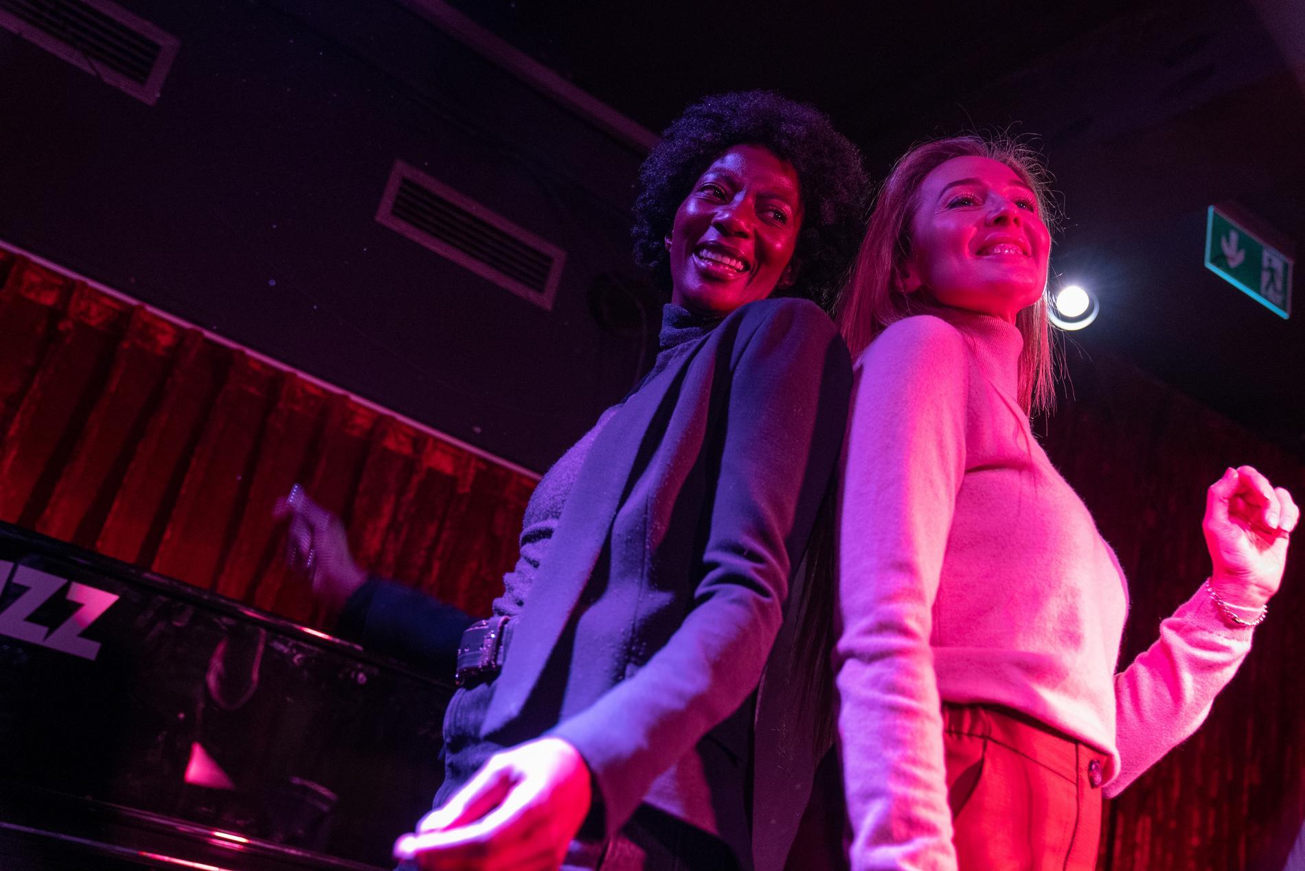 Zwei tanzende Frauen, angestrahlt von pinkem Club-Licht, in Frosch-Perspektive.